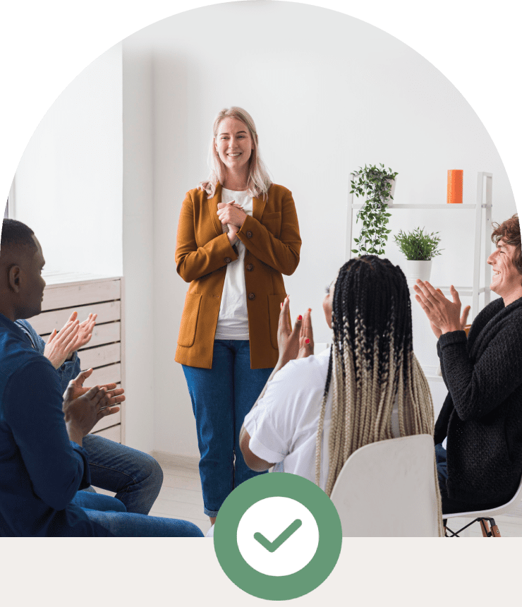 A woman presenting to an engaged, applauding group in a bright room.