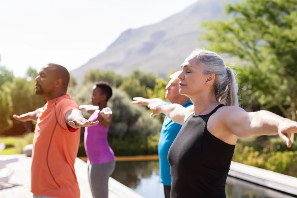 Group practicing yoga outdoors near mountains.