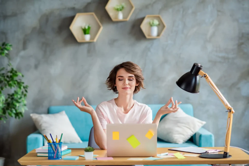 Woman meditating at desk with laptop.