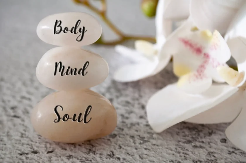 Stacked stones with words Body, Mind, Soul, and a white flower nearby.