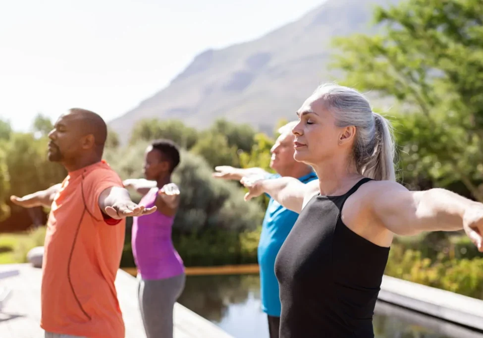 Group practicing yoga outdoors near mountains.