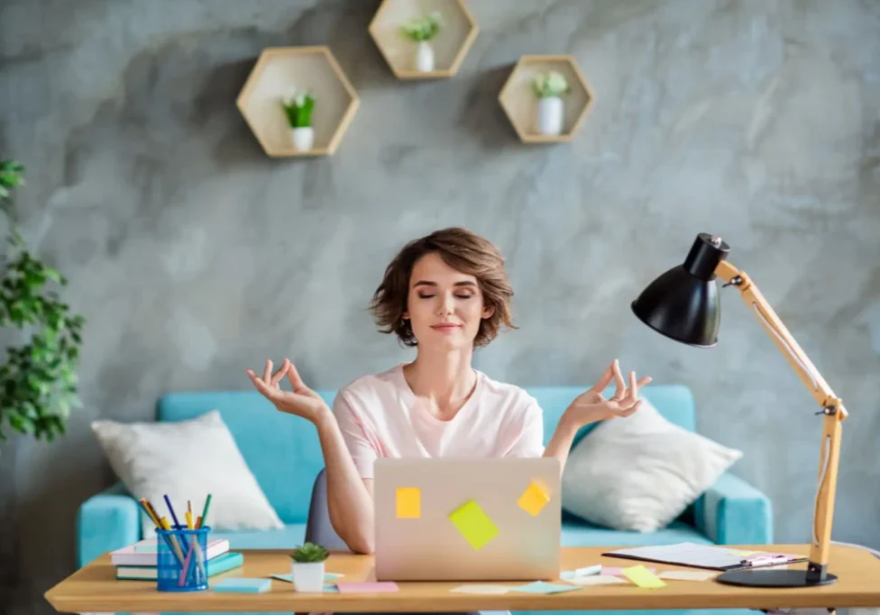 Woman meditating at desk with laptop.